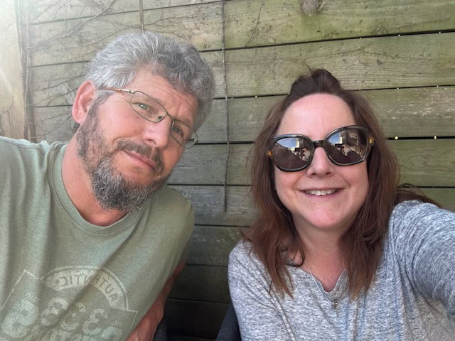 Smiling couple at Riverside Seasonal Campground taking a selfie outdoors, enjoying nature and camping amenities.